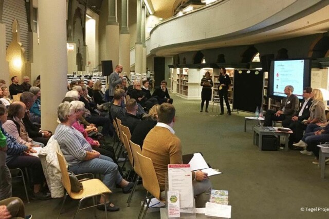 Menschen sitzen auf Stühlen und schauen einer Präsentation zu